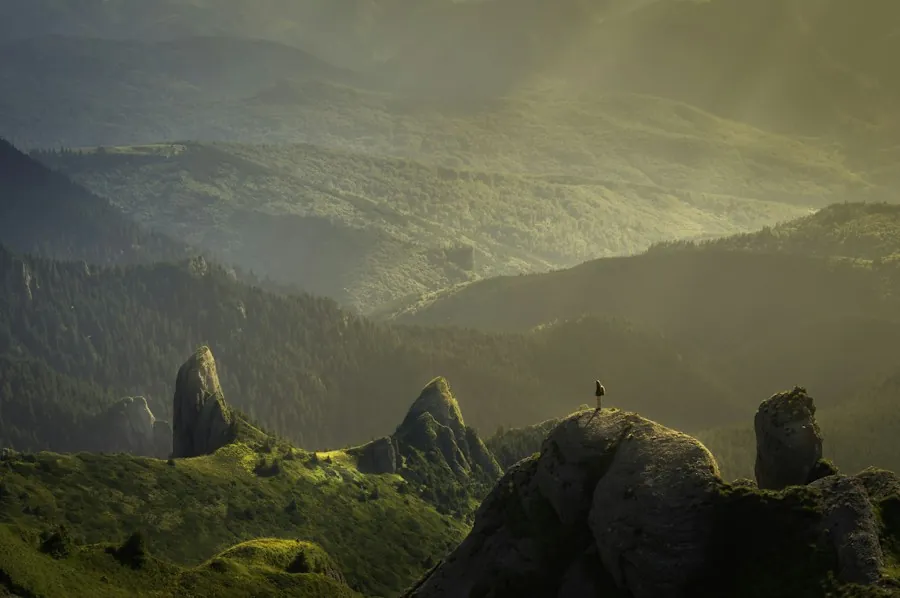 A small figure standing on a rocky peak above misty green valleys