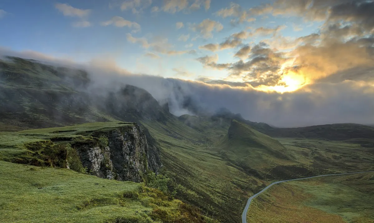 Misty green hills at sunrise with a winding road below