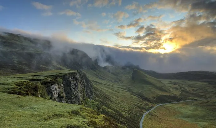 Misty green hills at sunrise with a winding road below