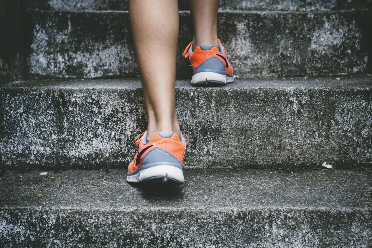 Close view of a person's legs and orange running shoes climbing concrete steps