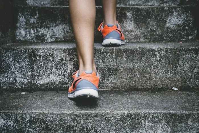 Close-up of a person in orange sneakers climbing concrete steps, part of a sustainable movement routine