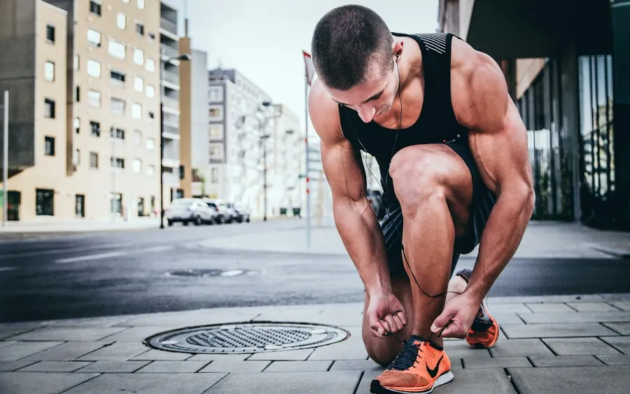 A runner crouching to tie an orange running shoe on a city street