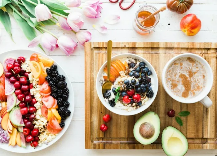 Bowls of fresh fruit and yogurt on a wooden board with an avocado and tulips