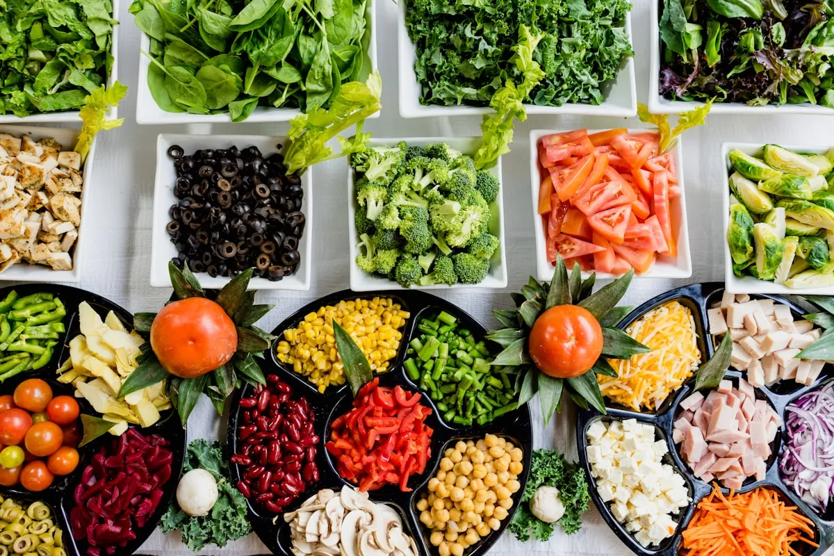 Overhead view of bowls filled with chickpeas, kidney beans, broccoli, olives, tomatoes and leafy greens