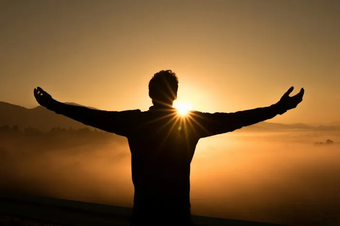 A person standing with open arms facing a glowing sunset