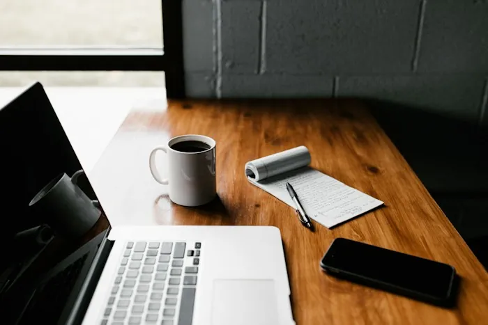A laptop, a coffee mug and a notepad on a wooden desk