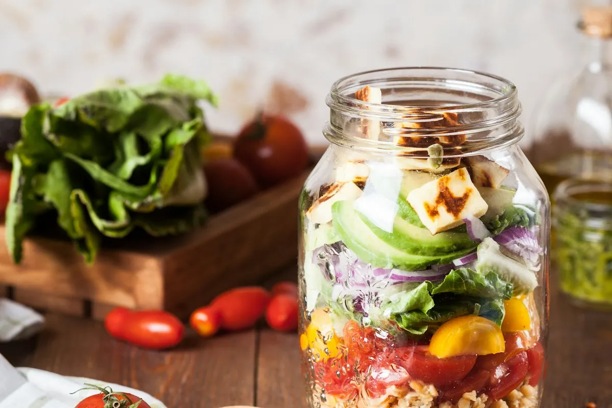 A glass jar layered with grains, avocado, vegetables and cheese for a make-ahead lunch