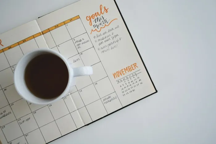 A monthly planner and a cup of coffee on a white desk