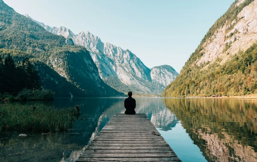A person sitting alone on a wooden dock looking over a calm mountain lake