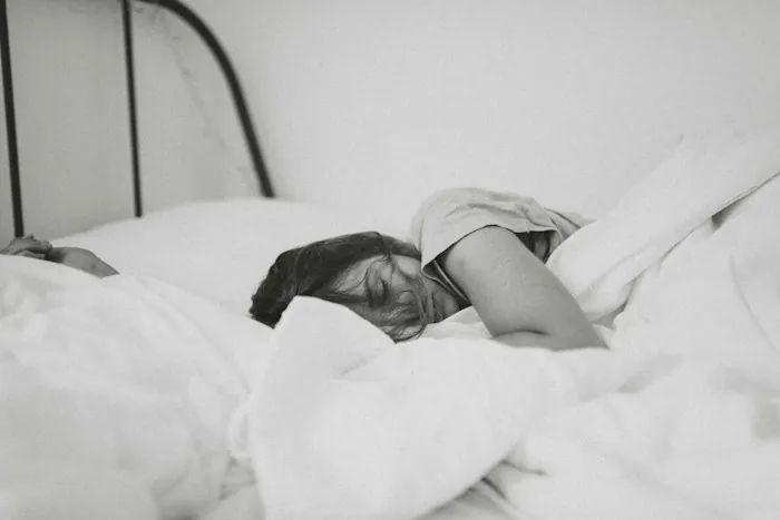 A person sleeping soundly in a white bed, shown in black and white