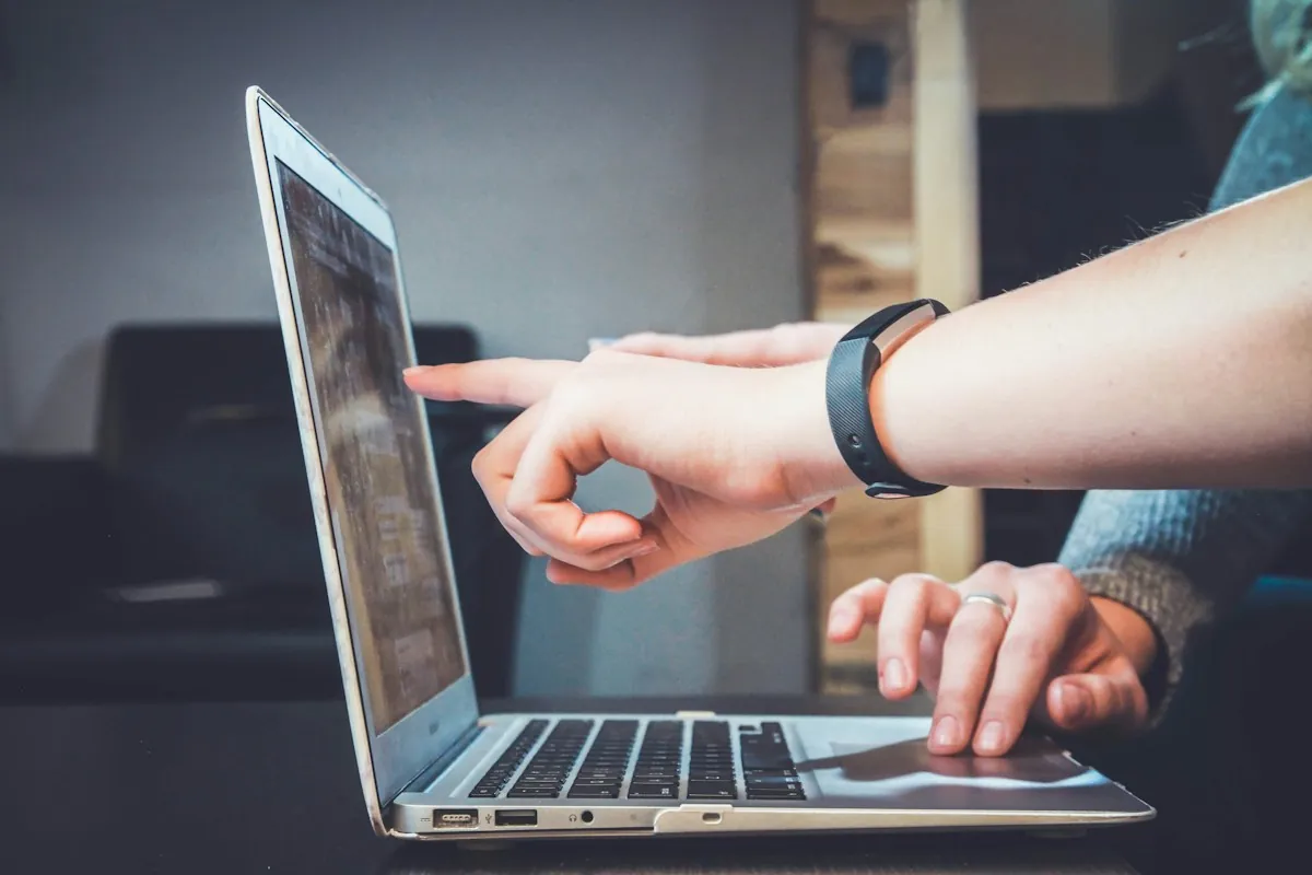 Hands pointing at a laptop screen, one wrist wearing a fitness band