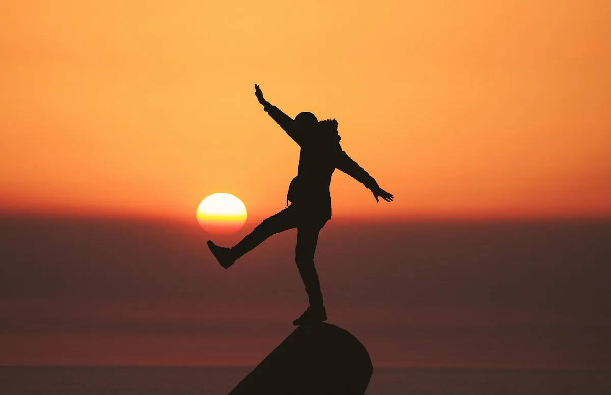 A person balancing on one leg on a rock at sunset
