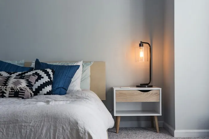 A bedroom with a made bed and a lit lamp on the bedside table