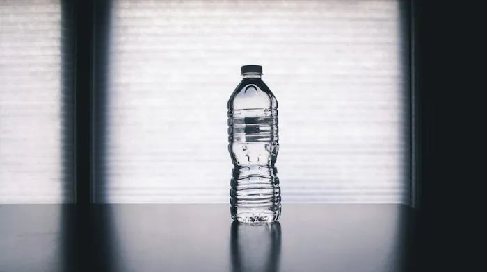 A clear bottle of water on a dark table in soft window light