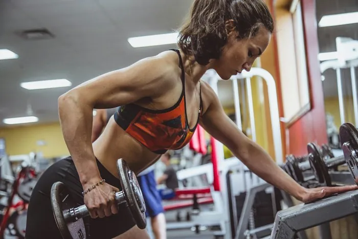 A woman in a gym leaning forward while lifting a dumbbell