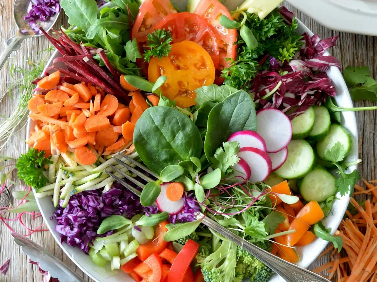 A large bowl of colorful fresh salad with tomatoes, radishes, carrots and leafy greens