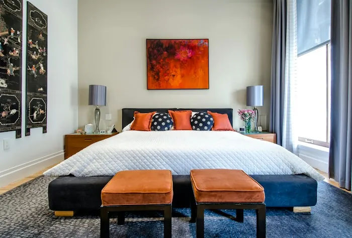 A bright bedroom with a made bed, a bench and a large window
