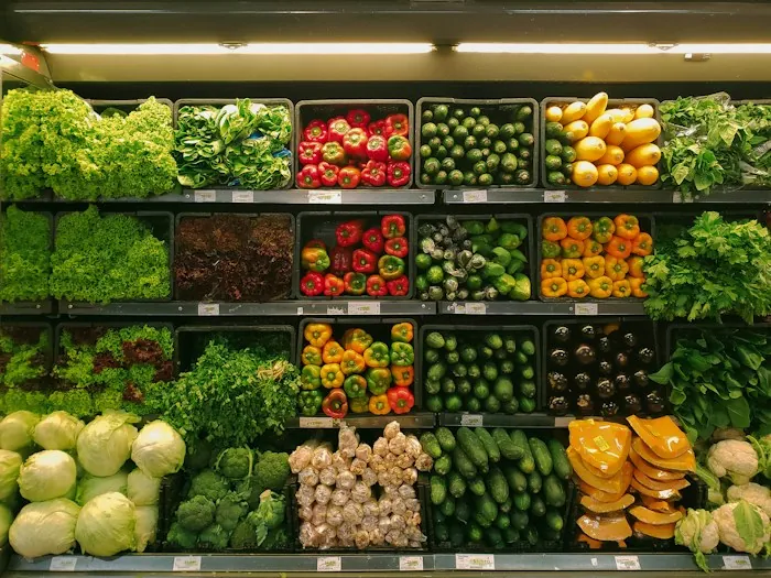 A grocery store shelf display of fresh lettuce, peppers, cucumbers, cabbage and broccoli
