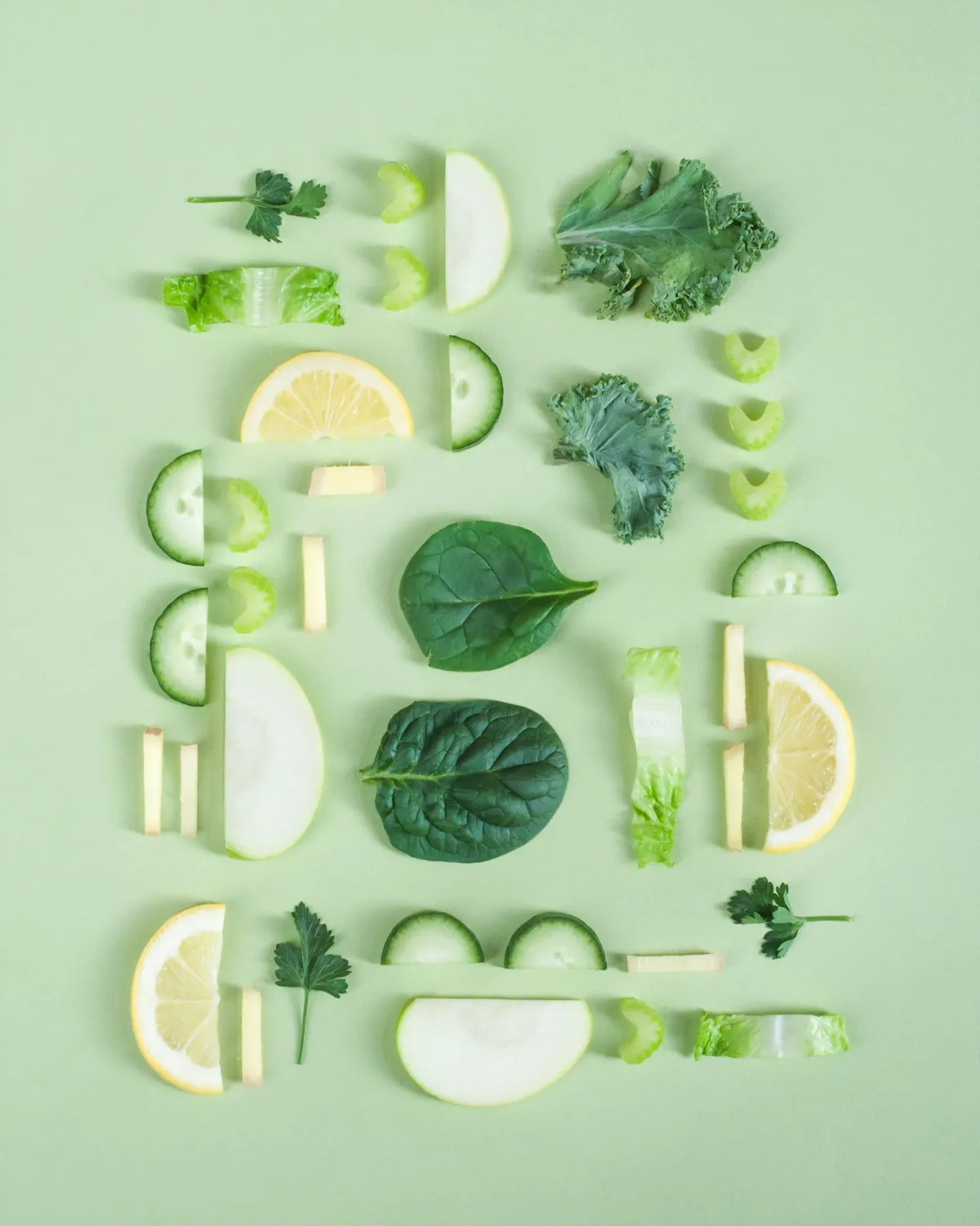 Fresh spinach, kale, cucumber and lemon slices arranged on a pale green background