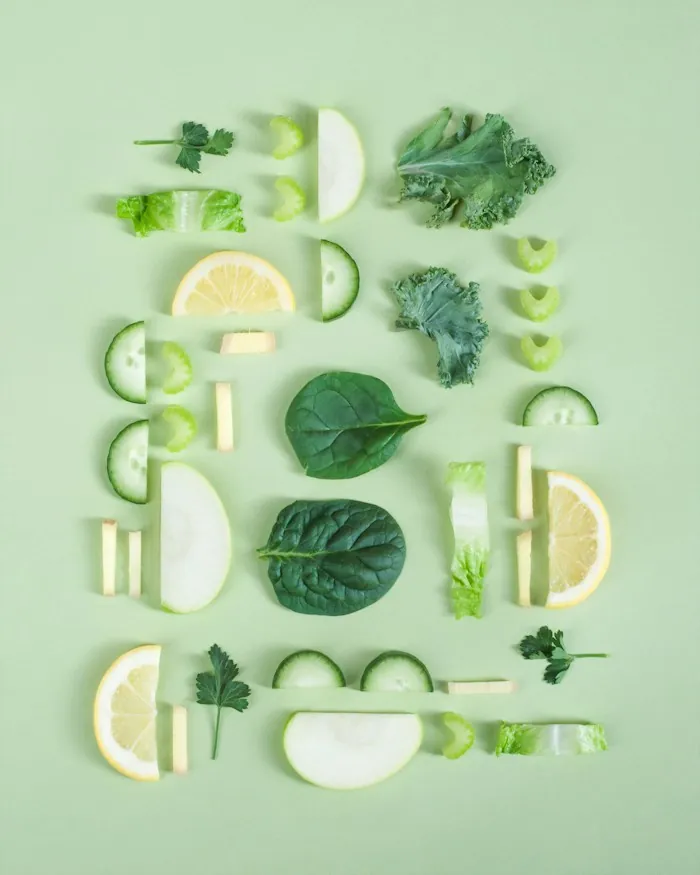 Fresh spinach, kale, cucumber and lemon slices arranged on a pale green background