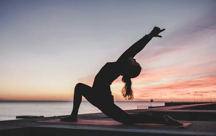 A silhouette of a person in a deep stretch outdoors at dusk
