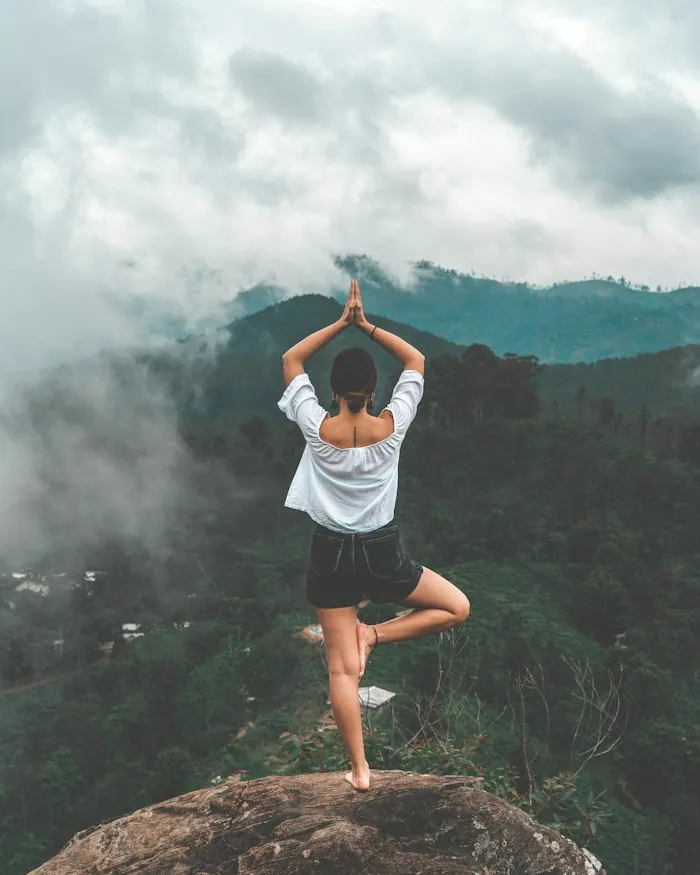 A person in a yoga tree pose above misty green hills