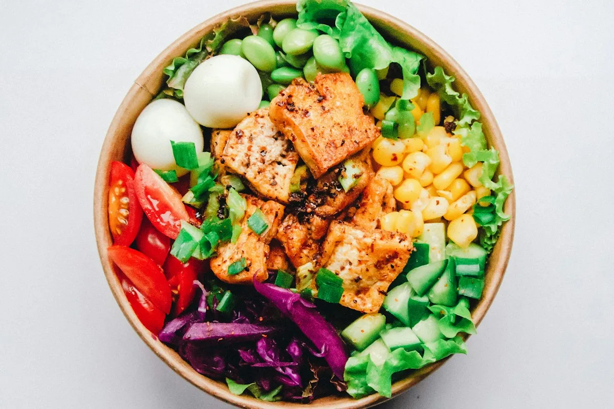 A bowl of salad with grilled chicken, egg, corn, cucumber and red cabbage