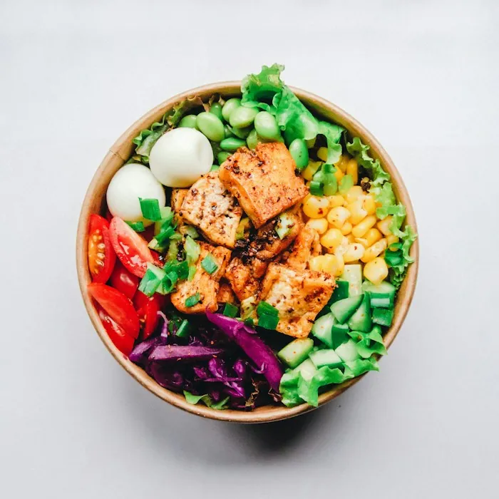 A wooden bowl with grilled chicken, egg, greens, corn and cucumber, a protein-rich meal