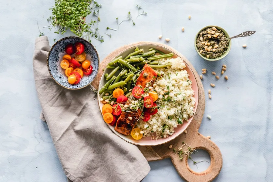 A plate of salmon, green beans, grains and cherry tomatoes on a wooden serving board