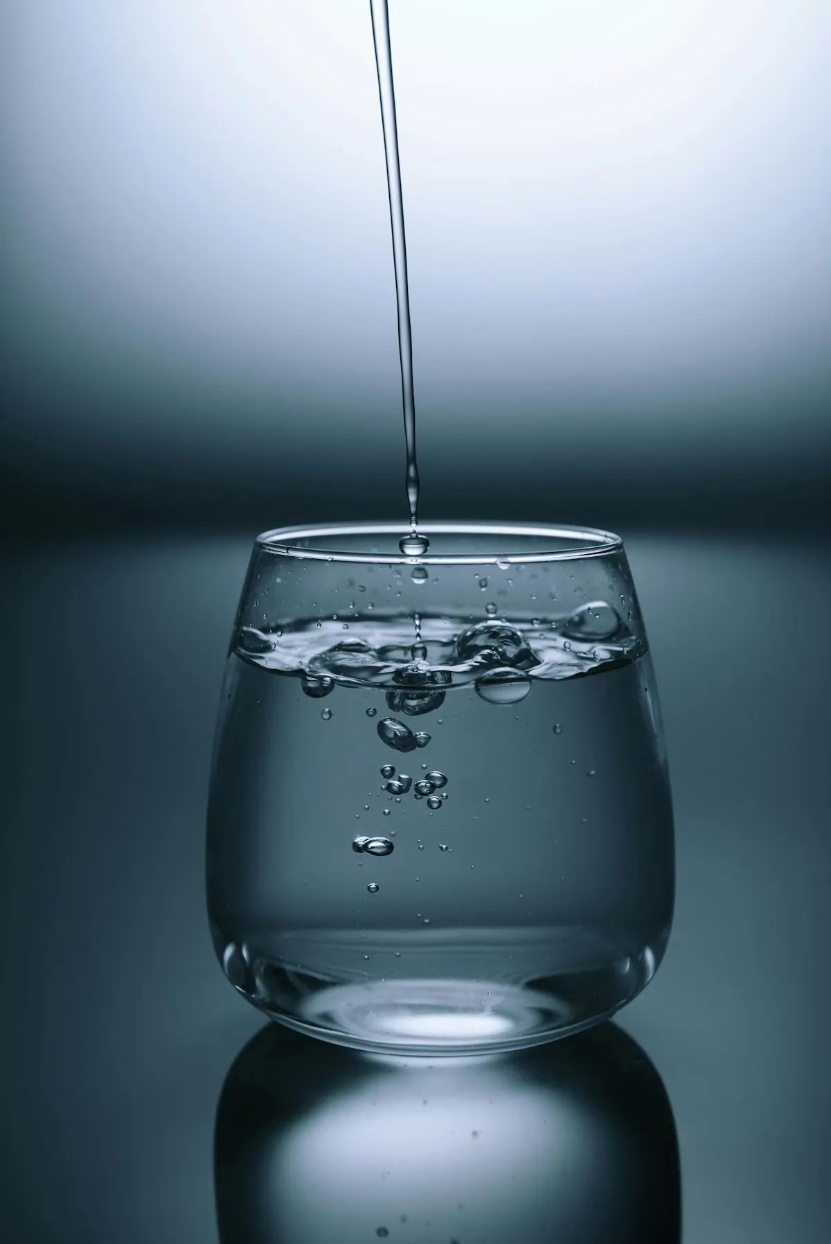 A clear glass being filled with water from a thin stream against a dark grey background