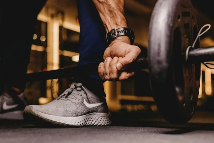 A hand gripping a barbell above a running shoe in a gym