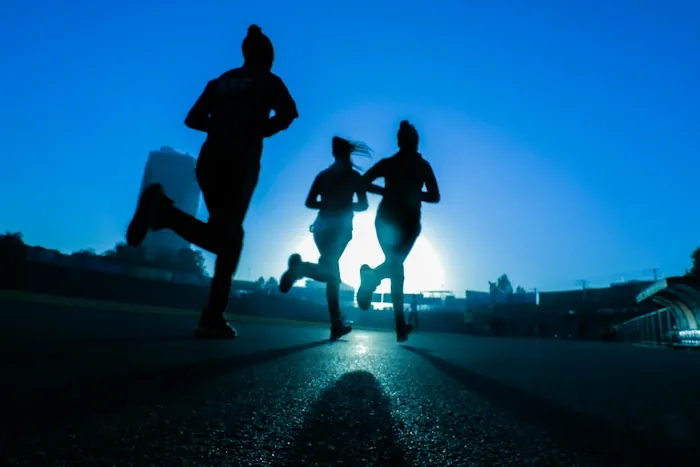 Three runners silhouetted against a bright sunrise on a city road