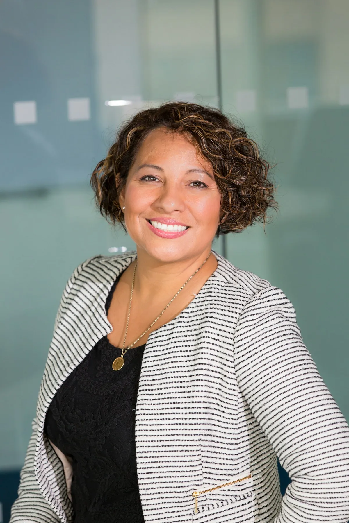 A smiling woman with short curly hair wearing a striped cardigan