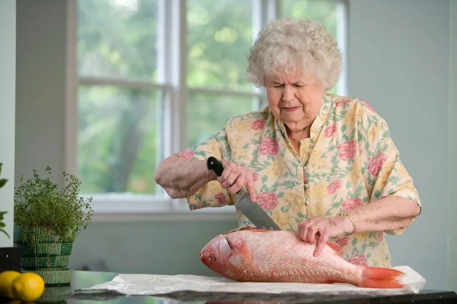 An older woman preparing a fish on a counter in a bright kitchen