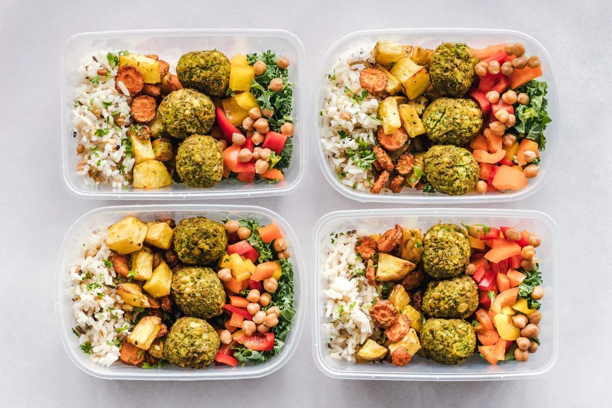 Four meal prep containers with rice, falafel, roasted vegetables and chickpeas