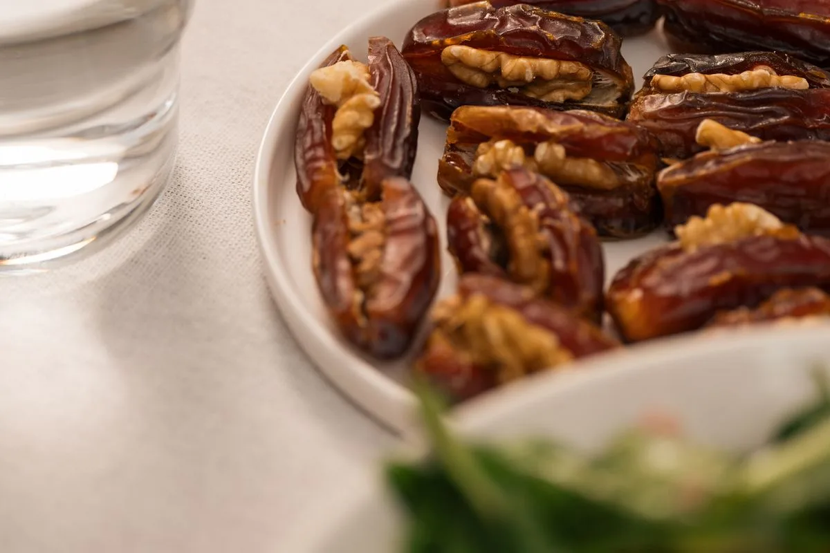 A plate of dates and walnuts beside a glass of water, a traditional way to break a fast gently