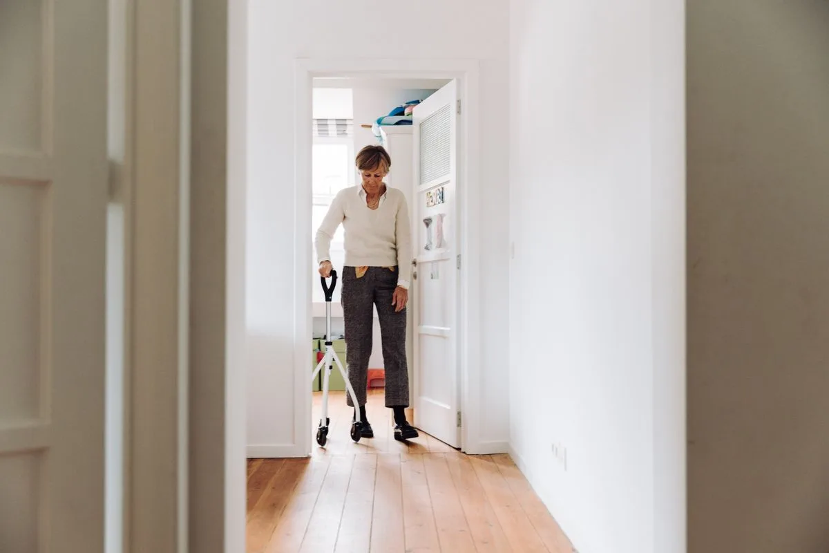 An older woman walking confidently with a mobility walker through a bright, clutter-free hallway