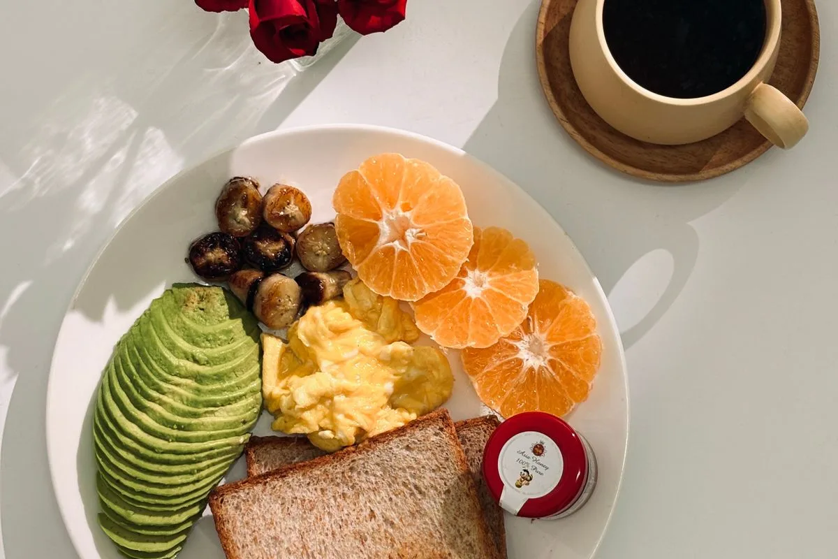 A balanced breakfast plate of avocado, eggs, orange and toast with coffee