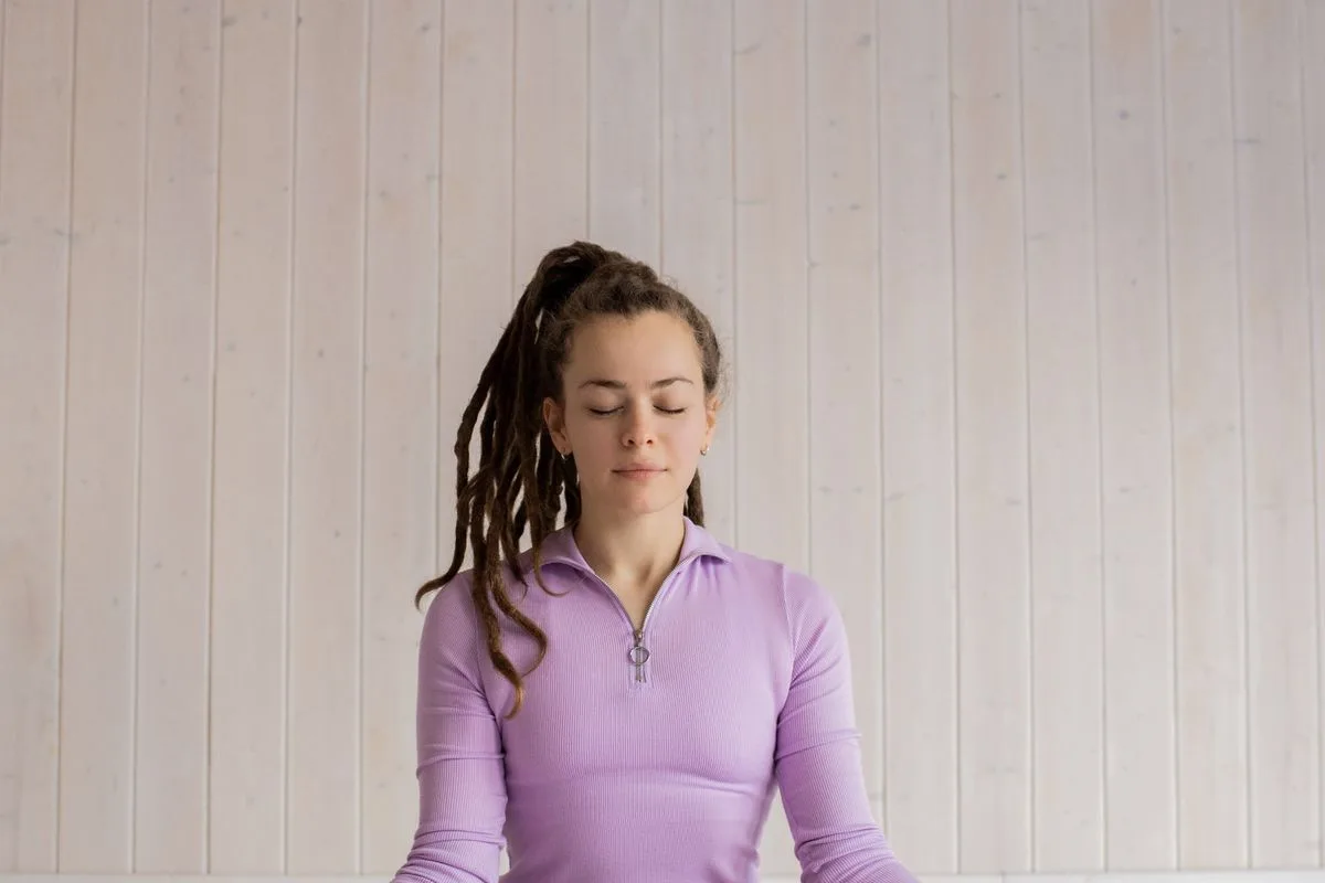 A woman sitting cross-legged on a mat with her eyes closed, practicing calm breathing