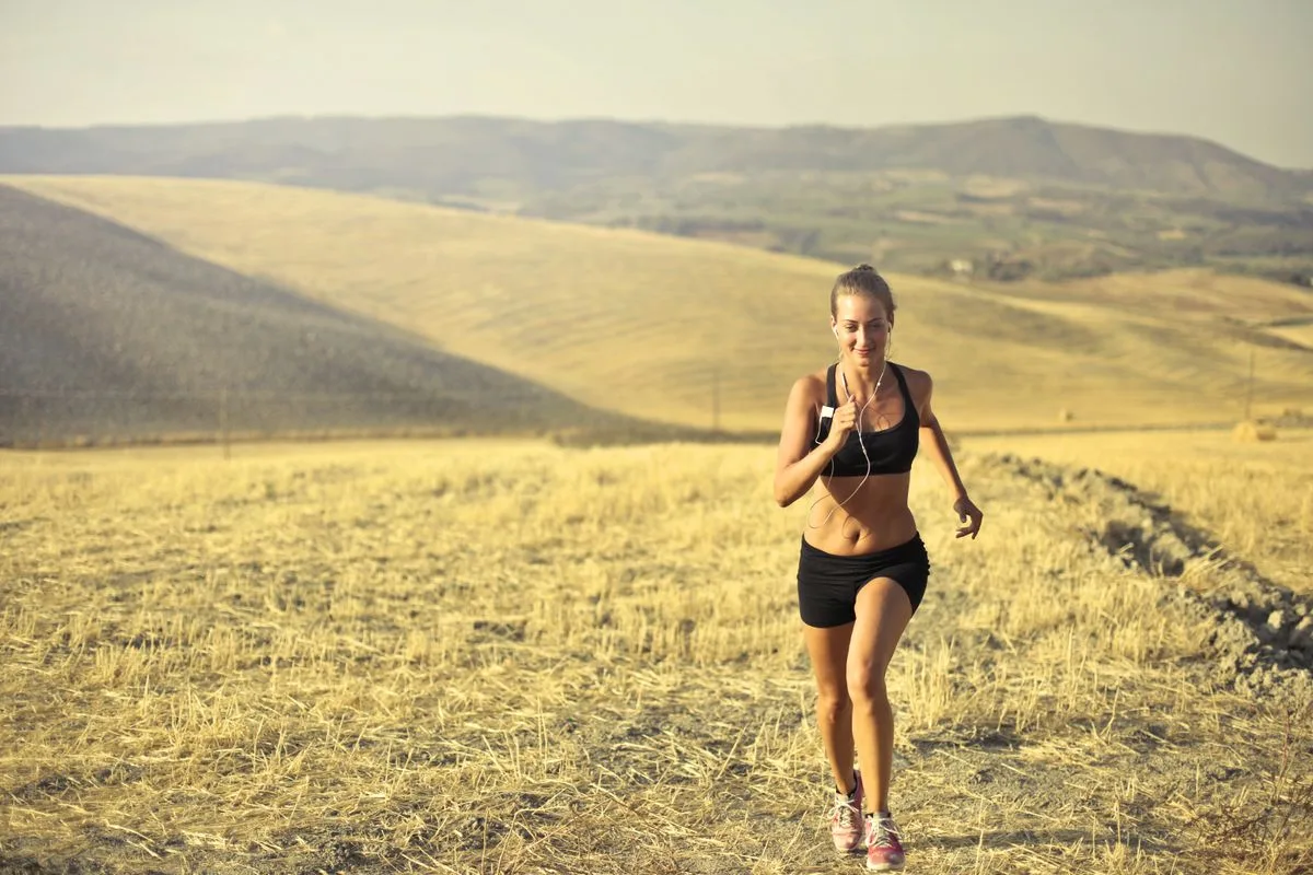 A woman running energetically along a sunlit hillside trail