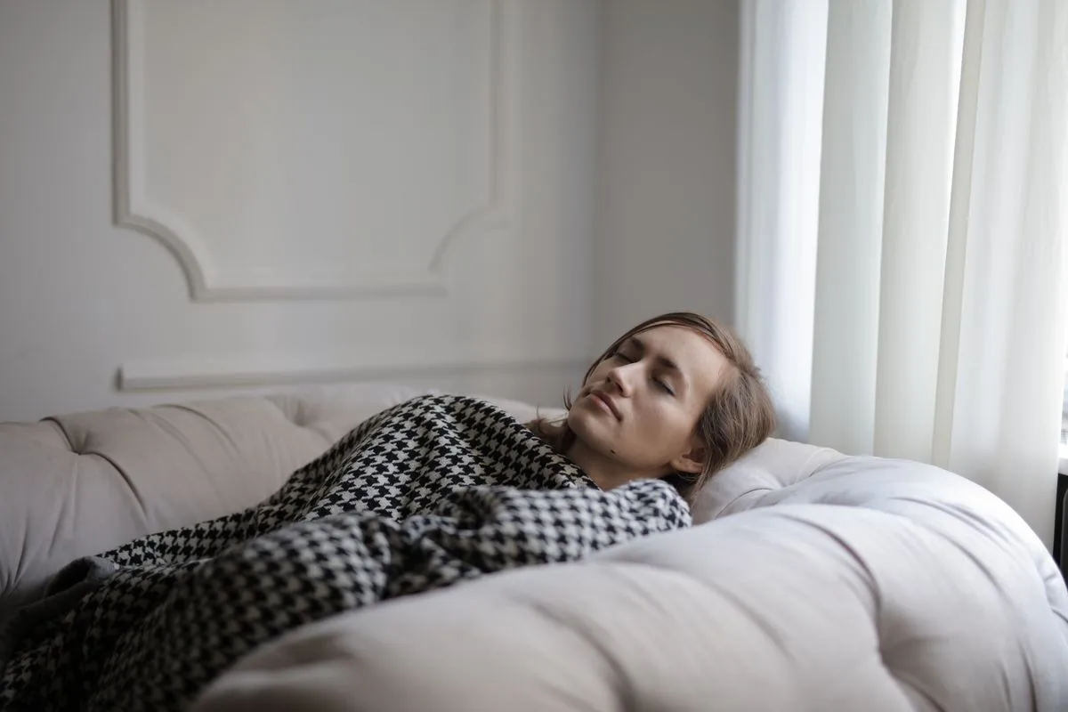 A woman resting comfortably under a blanket on a sofa during the day