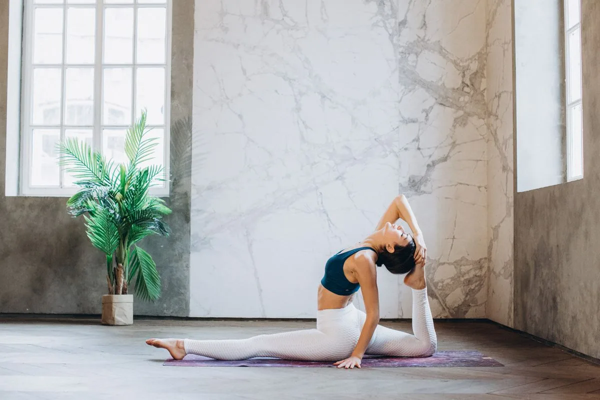 A woman in a deep seated backbend stretch opening her hip flexor and reaching overhead to extend her shoulder