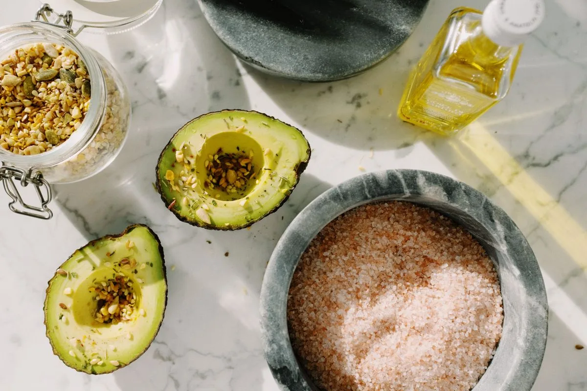 Avocado halves topped with seeds beside a jar of nuts and a bottle of oil