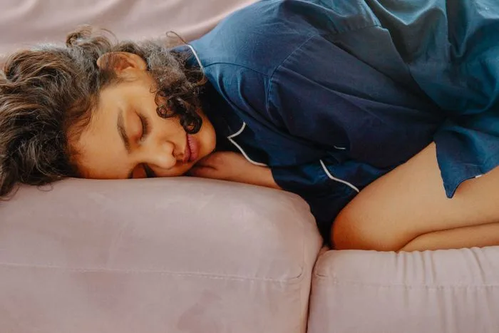 A woman napping peacefully on a sofa in daytime, wearing comfortable pajamas