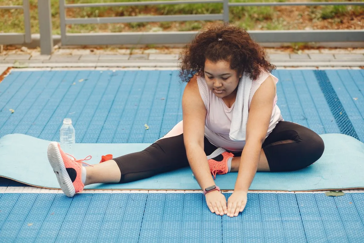 A woman seated on a mat stretching forward to open her hips and hamstrings