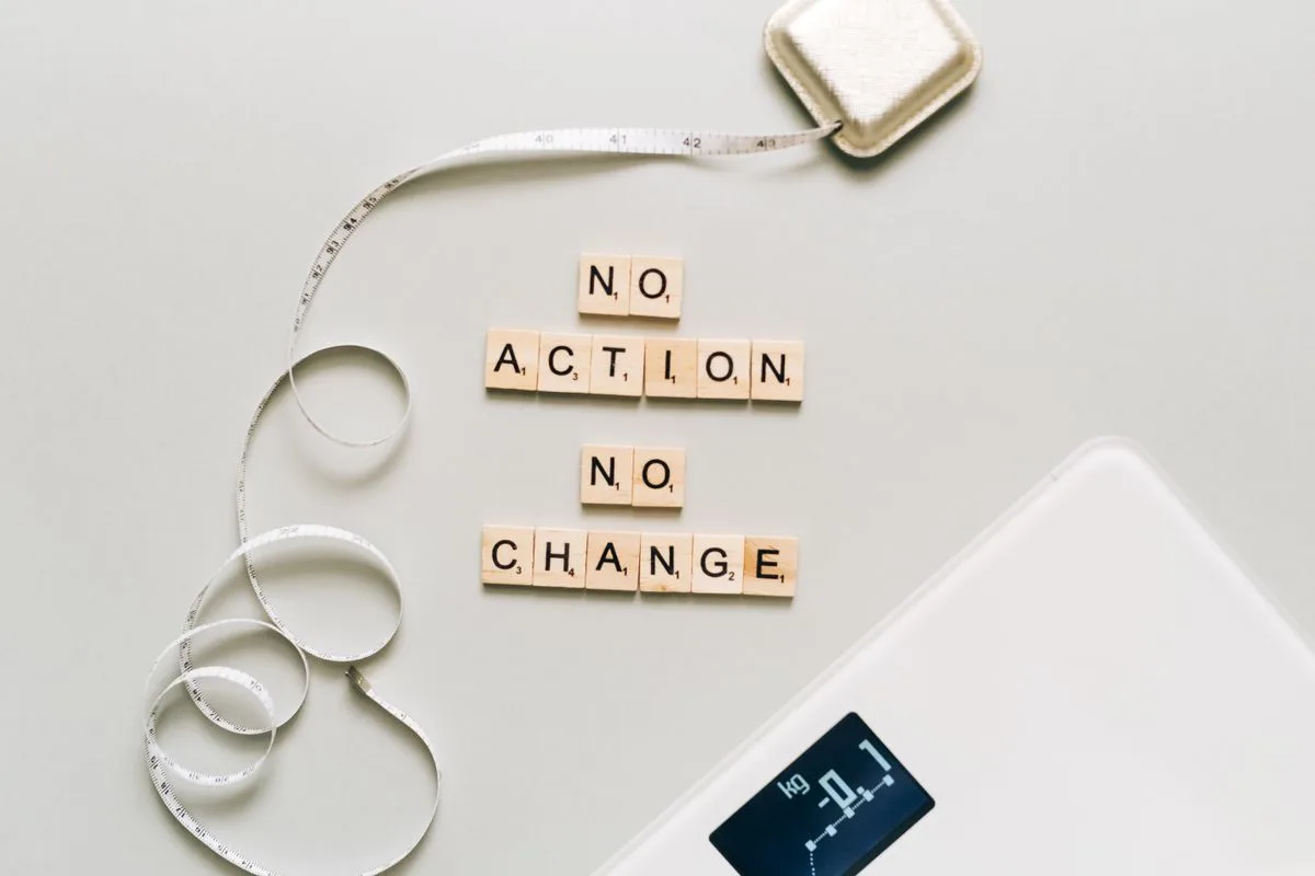 Wooden letter tiles spelling out 'no action no change' beside a measuring tape and scale