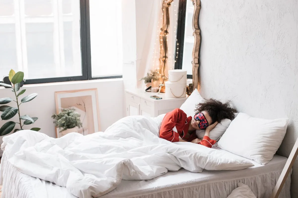 A woman resting peacefully in a cozy bed with a sleep mask among soft indoor plants