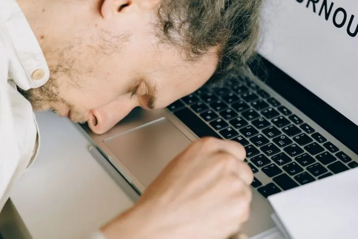 An exhausted person resting their head on a laptop keyboard at their desk