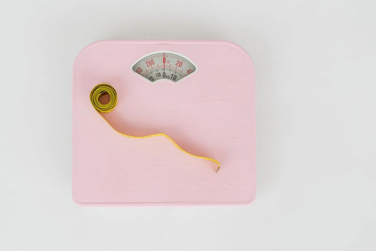 A pink bathroom scale with a measuring tape coiled on top, viewed from above