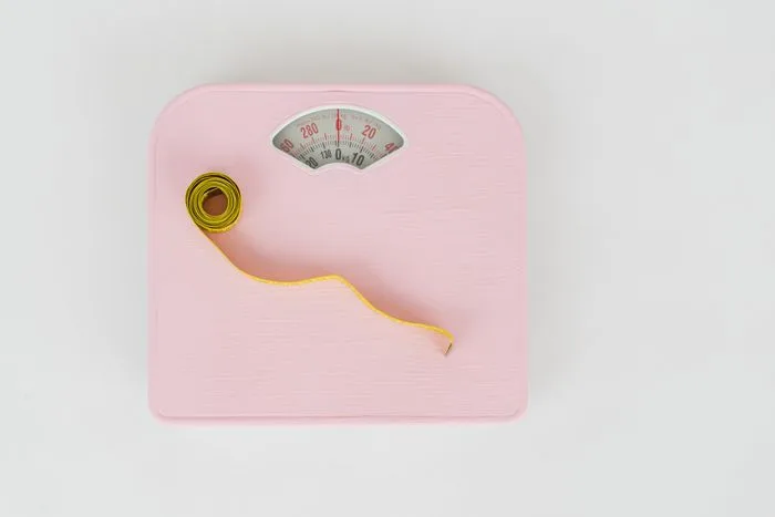 A pink bathroom scale with a measuring tape coiled on top, viewed from above